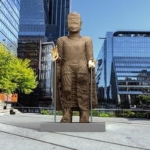 Sculpture monumentale dorée installée sur une place entre des gratte-ciel